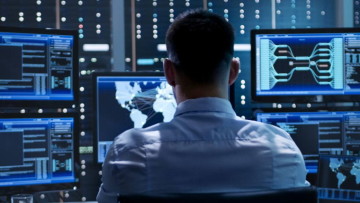 man sitting in front of multiple desktop monitor screens